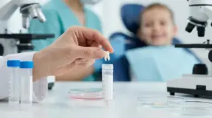 Ricercatore in laboratorio tiene un dente da latte sopra una provetta; sullo sfondo un bambino dal dentista sfocato