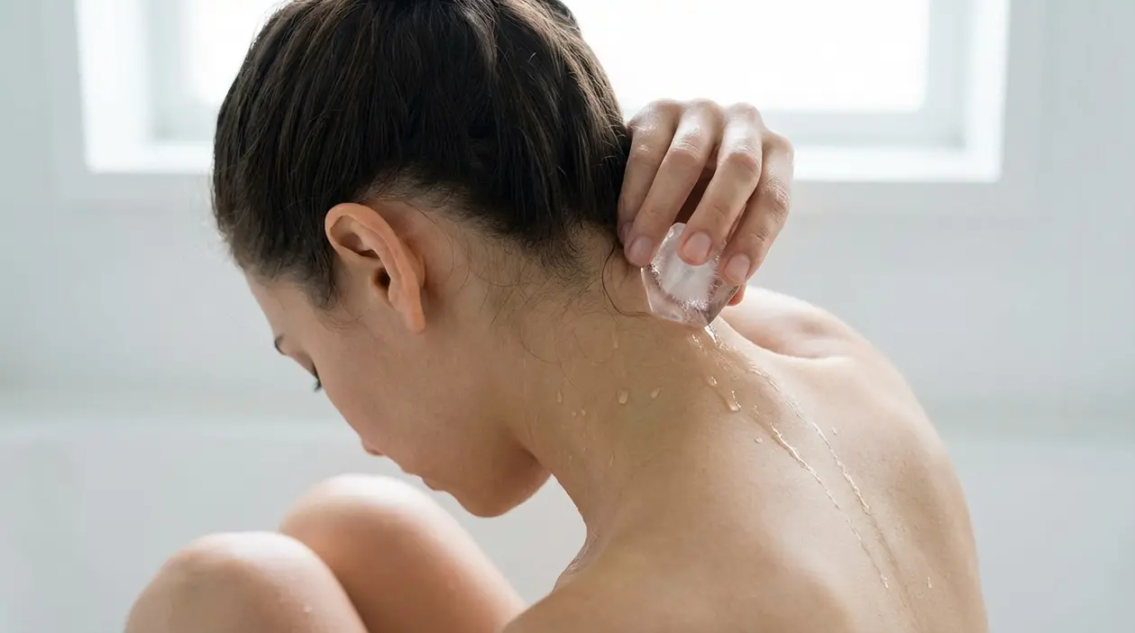 Persona che applica un cubetto di ghiaccio alla base del collo, sul retro della testa