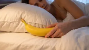Persona sdraiata a letto con una banana in mano vicino al cuscino, simbolo di un rimedio naturale per dormire meglio