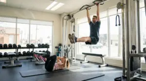 Persona alla sbarra esegue sollevamento gambe e persona sul tappetino fa crunch in palestra