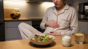 Persona in pigiama con mano sulla pancia davanti a un’insalata serale in cucina