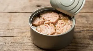 Scatoletta di tonno aperta con tranci di tonno conservati in olio su un tavolo di legno