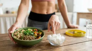 Persona indica una ciotola di zucchero accanto a un pasto sano per favorire una pancia piatta