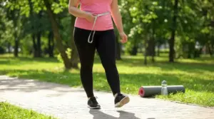 Persona che cammina nel parco con metro in vita, immagine legata a dimagrimento addominale e attività fisica