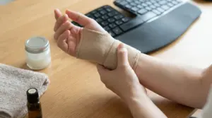 Persona con polso fasciato che massaggia la mano su una scrivania, contesto di dolore da tunnel carpale