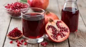 Bicchiere di succo di melograno con frutti freschi e chicchi su un tavolo di legno