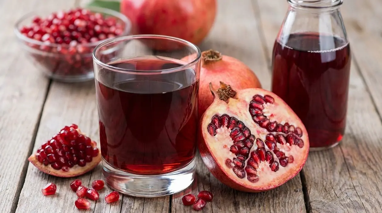 Bicchiere di succo di melograno con frutti freschi e chicchi su un tavolo di legno