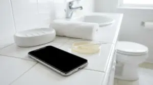 Smartphone appoggiato sul lavabo del bagno vicino a sapone e asciugamano, con WC sullo sfondo