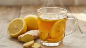 Tisana calda zenzero e limone in tazza di vetro con fette di limone e zenzero su tavolo in legno