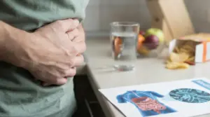 Persona con le mani sull’addome accanto a bicchiere d’acqua e illustrazione dell’apparato digerente