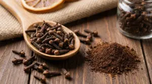 Chiodi di garofano interi in un cucchiaio di legno e polvere di chiodi di garofano su tavolo rustico